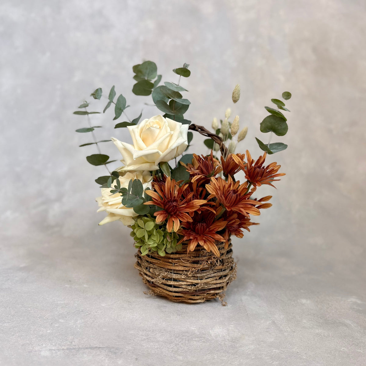 Gathered Basket, a rustic fall flower arrangement featuring warm autumn blooms, creamy roses, seasonal greenery and textural accents. Available for local flower delivery in the lehigh valley and surrounding areas