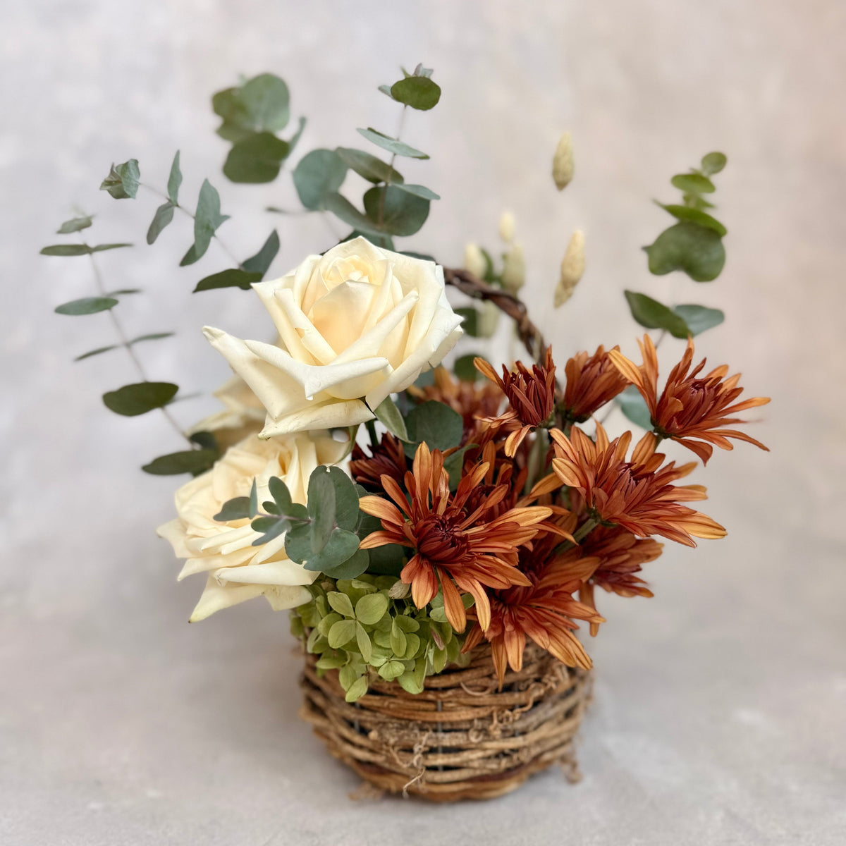 Gathered Basket, a rustic fall flower arrangement featuring warm autumn blooms, creamy roses, seasonal greenery and textural accents. Available for local flower delivery in the lehigh valley and surrounding areas