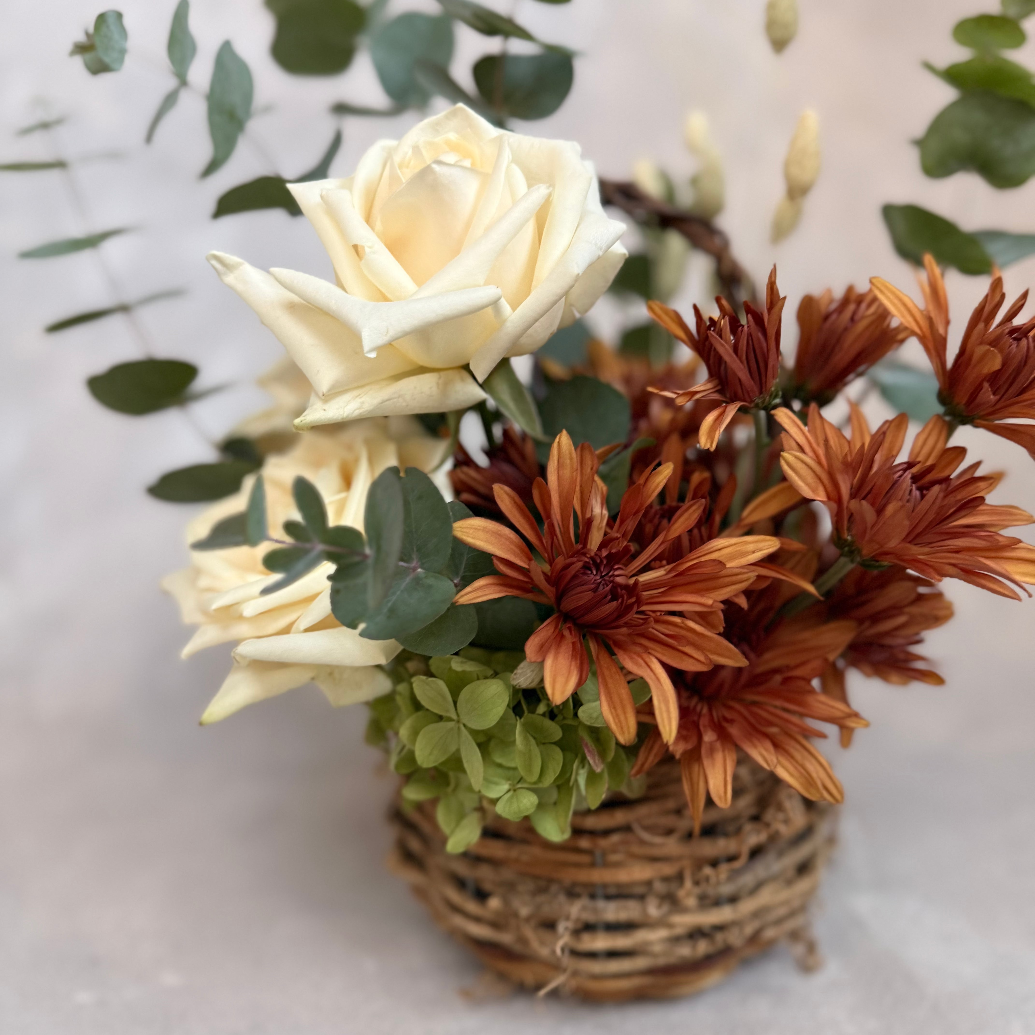 Gathered Basket, a rustic fall flower arrangement featuring warm autumn blooms, creamy roses, seasonal greenery and textural accents. Available for local flower delivery in the lehigh valley and surrounding areas